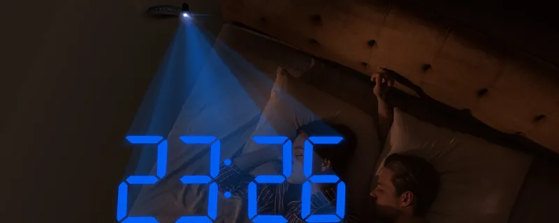 The time projected in blue on the wall above a bed at night