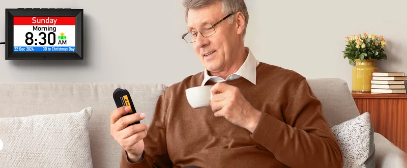 Talking day clock on the wall, a man on the sofa holding its remote